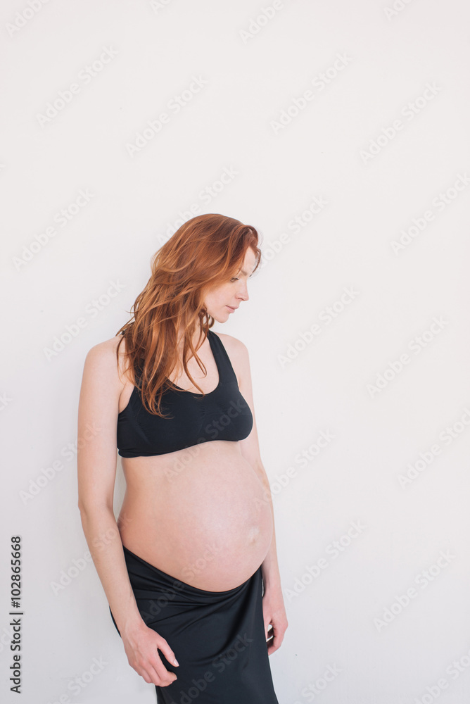 Pregnant woman with red hair in black clothes on a white wall Pregnant woman with red hair in black clothes on a white wall