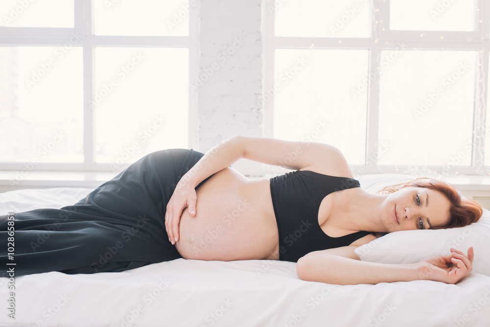Happy pregnant woman lying on the white sheet thoughtfully Happy pregnant woman lying on the white sheet thoughtfully