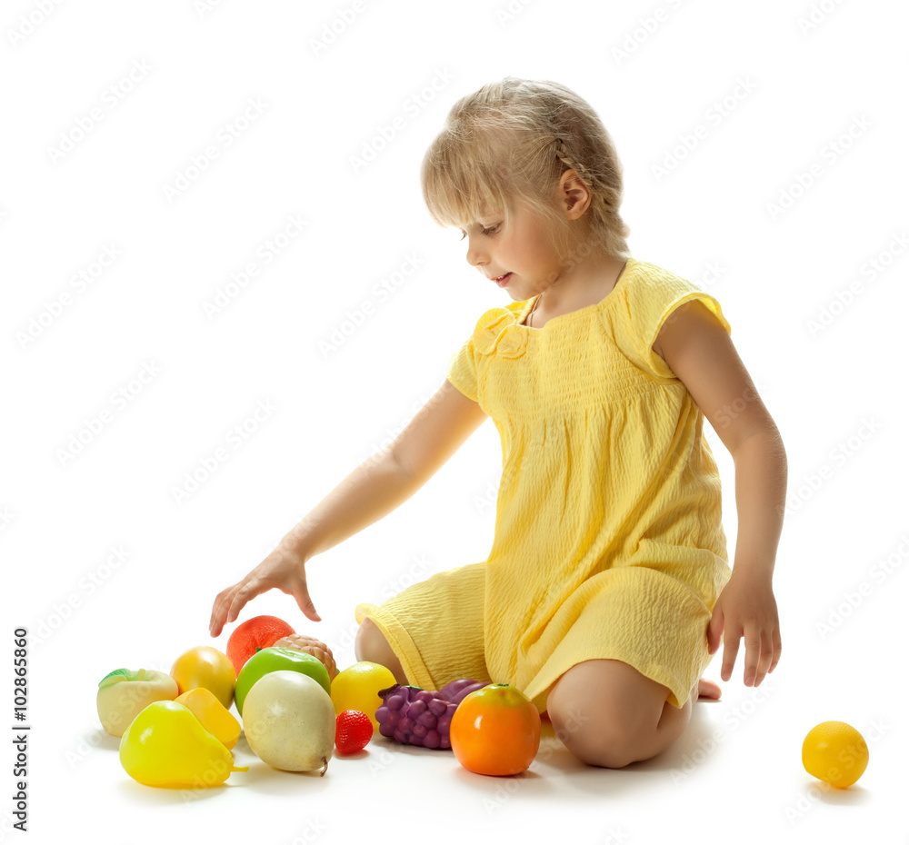 Charming little blonde girl in a yellow summer dress, sitting on her knees on the floor and plays with plastic toys - Isolated on white background Charming little blonde girl in a yellow summer dress, sitting on her knees on the floor and plays with plastic toys - Isolated on white background