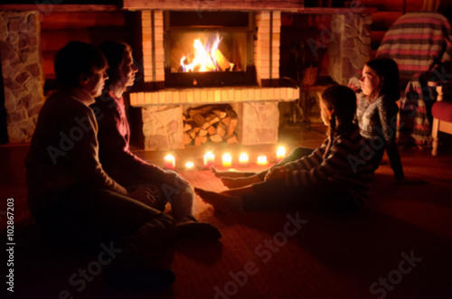 Blurred image of family sitting near fireplace in house, parents and kids relaxing near fire 