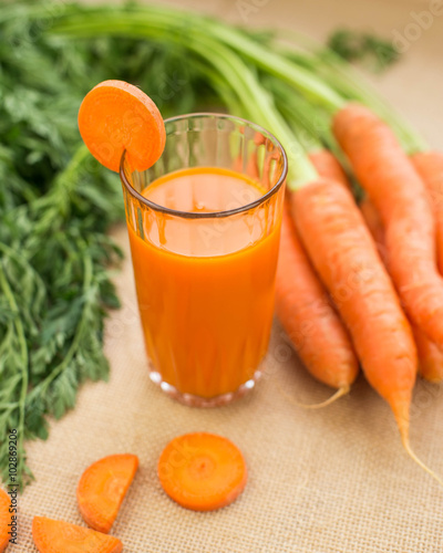 Fresh-squeezed carrot juice with vegetables on rustic background close up.