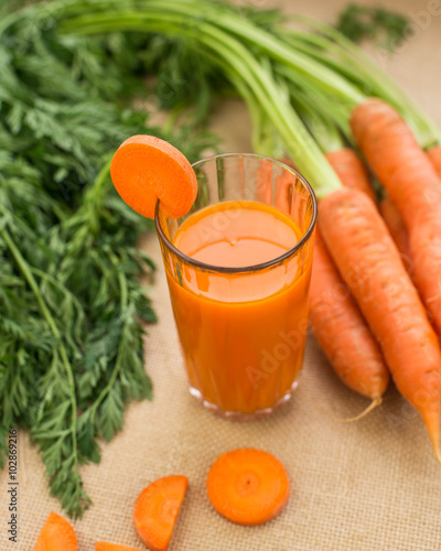 Fresh-squeezed carrot juice with vegetables on rustic background close up.
