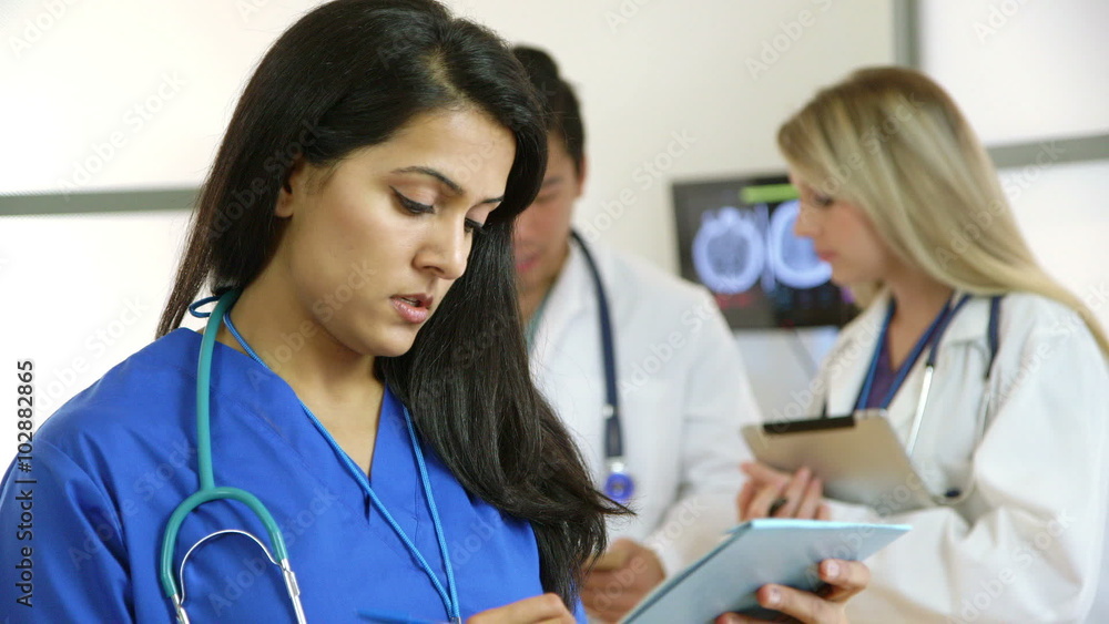 A nurse with other members of the medical team in background evaluates test results in a file. Scene dollies right.