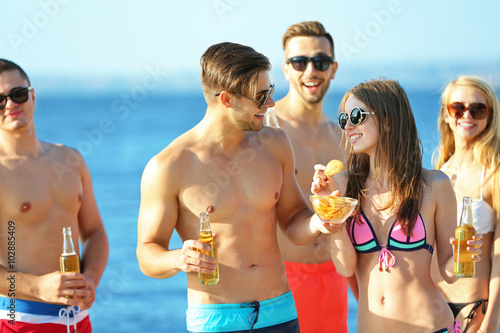 Happy young friends drinking beer at the beach  outdoors