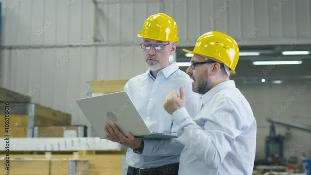 Two employees at logistics center warehouse are discussing work while holding a laptop computer. Shot on RED Cinema Camera. Two employees at logistics center warehouse are discussing work while holding a laptop computer. Shot on RED Cinema Camera.