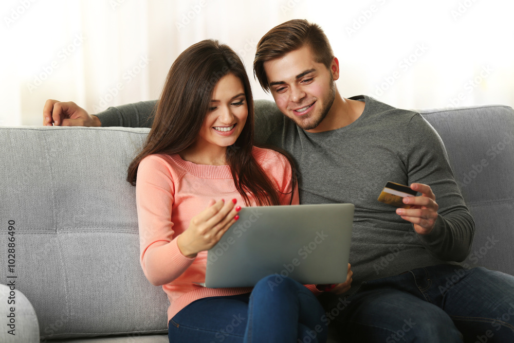 Young happy couple using credit card with laptop at home on light background Young happy couple using credit card with laptop at home on light background