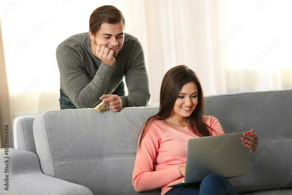 Young happy couple using credit card with laptop at home on light background Young happy couple using credit card with laptop at home on light background