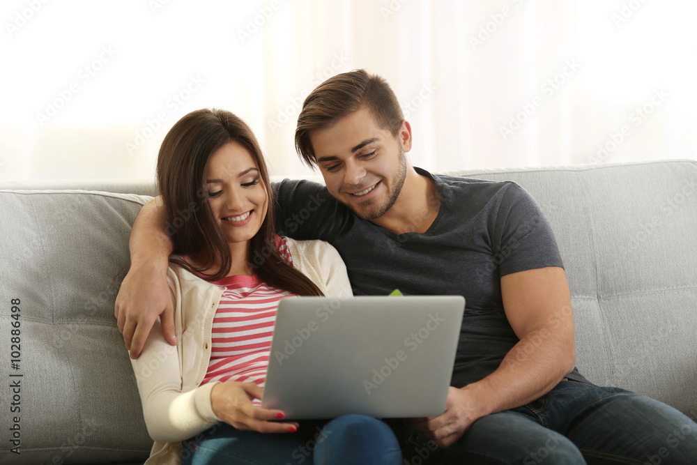 Young happy couple using credit card with laptop at home on light background