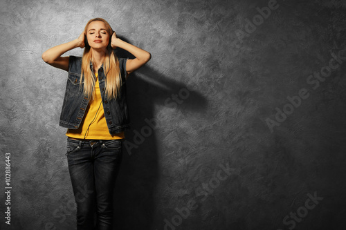 Young woman dancing and listening to music on grey wall background