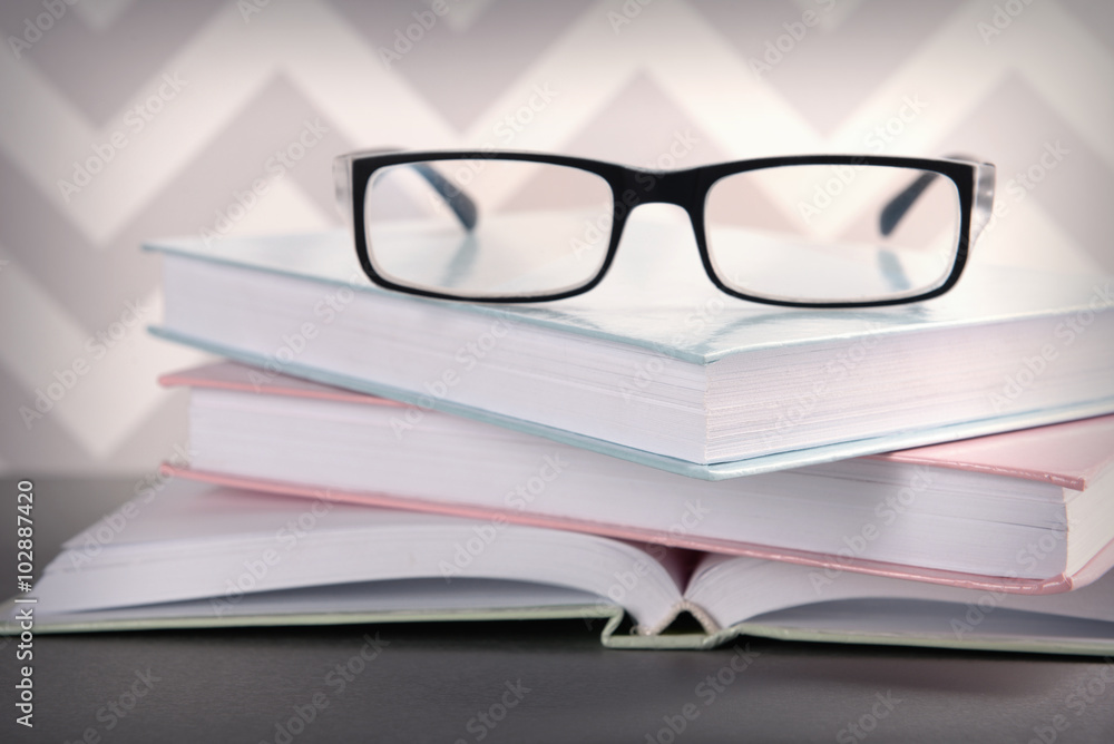 Books and eyeglasses on grey table against ornament wall, close up Books and eyeglasses on grey table against ornament wall, close up