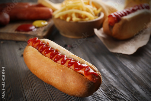 Hot dog with fried potatoes and fresh sausages on wooden background