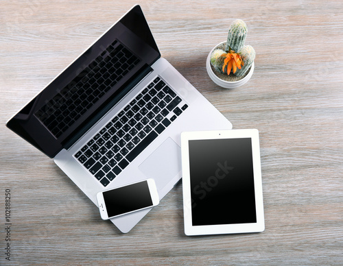 Modern laptop, smart phone and tablet with cactus on a wooden table