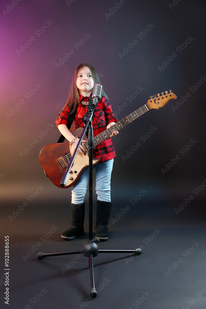 Fototapeta premium Beautiful little girl with microphone and guitar on dark purple background