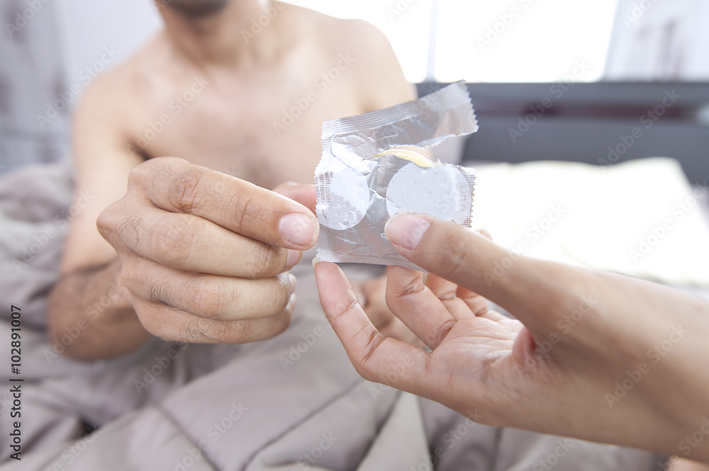 © arhendrix - Young woman opening condom and giveto a man in bed