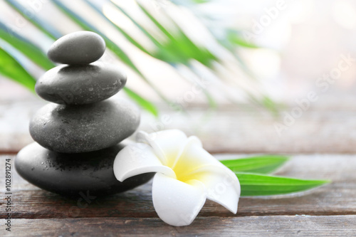Spa stones with bamboo, palm leaves and tropical flower on wooden background