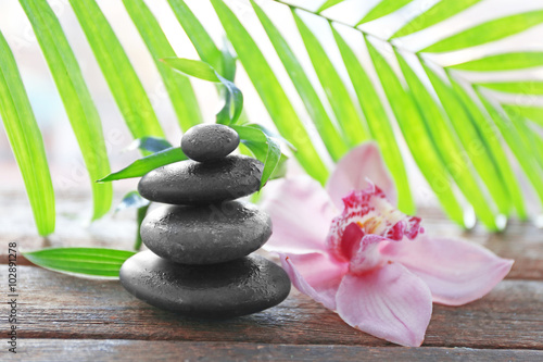 Spa stones with palm leaves and pink orchid on wooden background