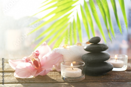 Spa stones with towel, candles, palm leaves and pink orchid on wooden background
