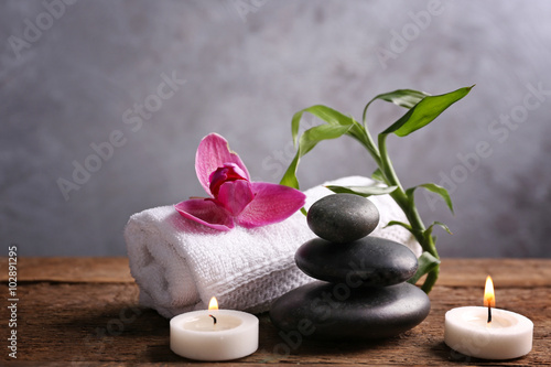Spa stones with candles  purple orchid  bamboo and towel on wooden table against grey background