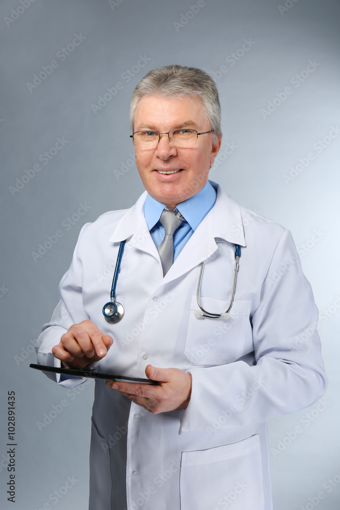 A handsome doctor with stethoscope and tablet standing on grey background A handsome doctor with stethoscope and tablet standing on grey background