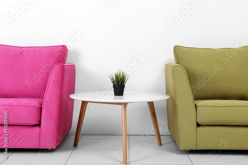 Living room interior with pink, green armchairs, white table and plant on white wall background