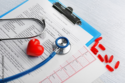 A stethoscope, pills, plastic heart and clipboard, close-up