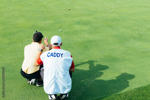 Golfer and caddy reading green photo