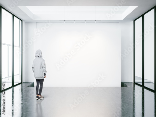 Young woman in empty modern gallery looking at the blank canvas. 
