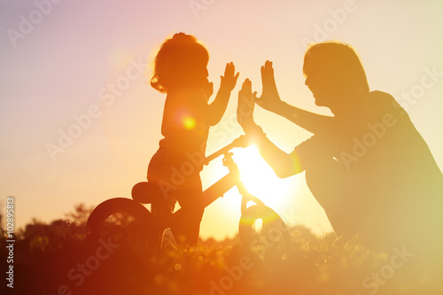 father and daughter having fun riding bike at sunset