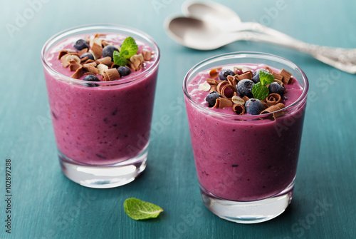 Healthy breakfast of smoothie, dessert, yogurt or milkshake with frozen blueberry and oats decorated grated chocolate and mint leaves on wooden rustic table