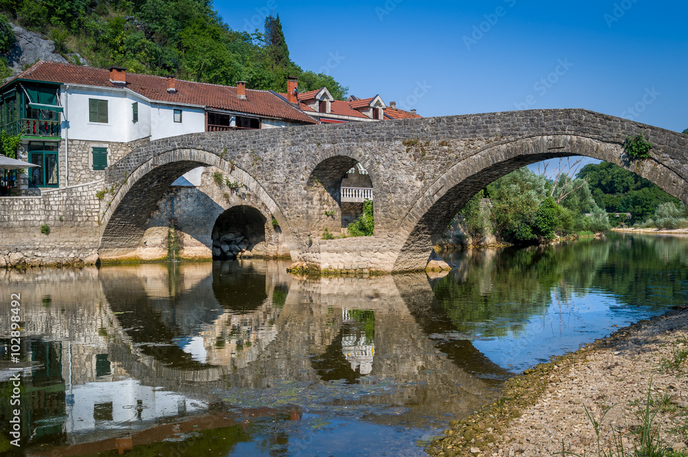 Rijeka Crnojevica old bridge panoraic view with reflections on the calm river waters.