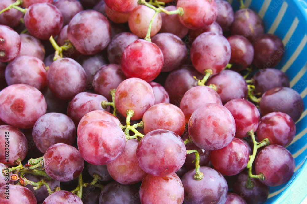 Red grape berries in blue basket on straw tray closeup Red grape berries in blue basket on straw tray closeup