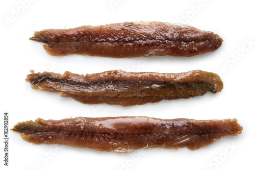 Three anchovy fillets with oil arranged symmetrically and isolated on white from above.