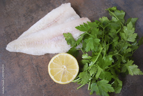 Frozen Alaska Pollock fillet with lemon and parsley. Preparation for cooking.