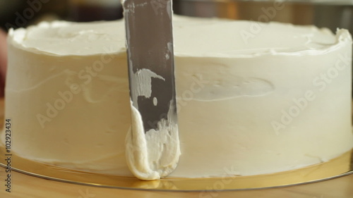 A baker spreads cream on a round cake while he spins it