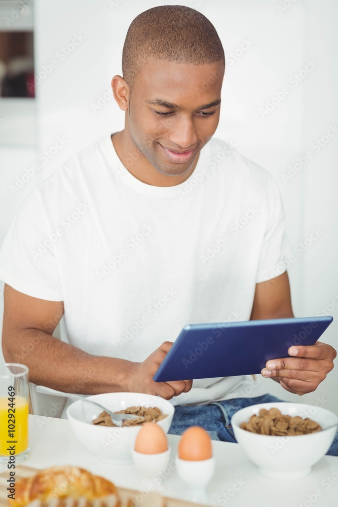 Young man using tablet and eating breakfast in kitchen Young man using tablet and eating breakfast in kitchen
