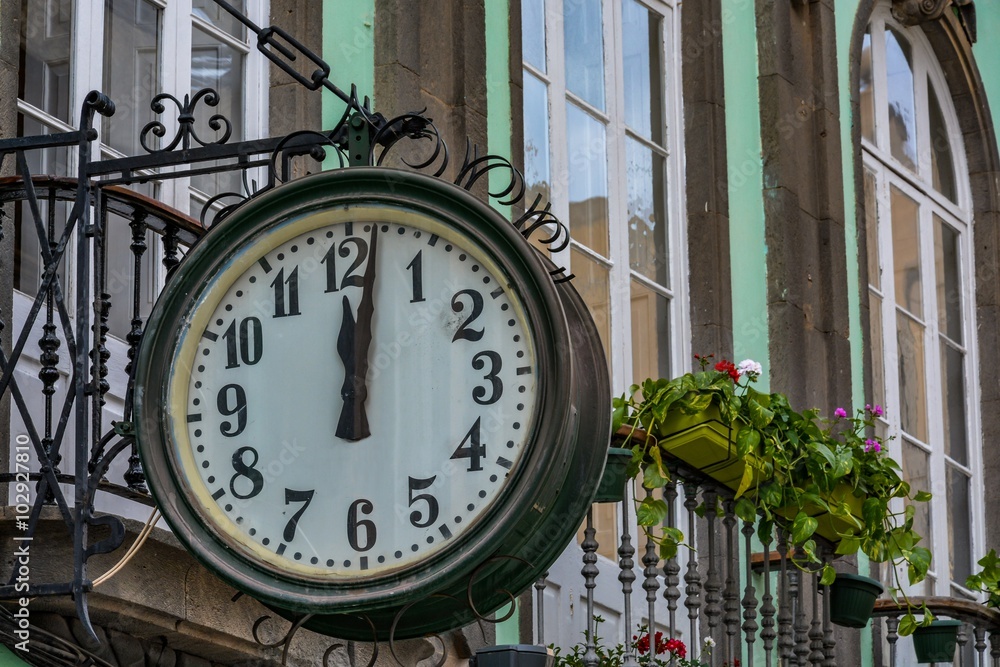 Traditional clock at a building showing 'just after noon'