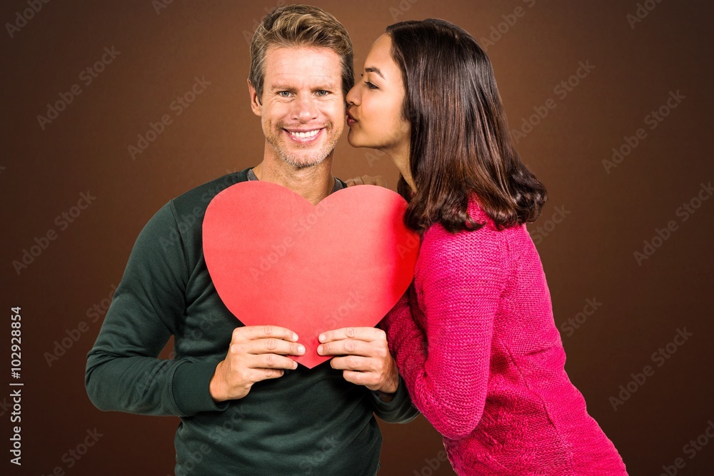 Composite image of woman kissing boyfriend with red heart shape 
