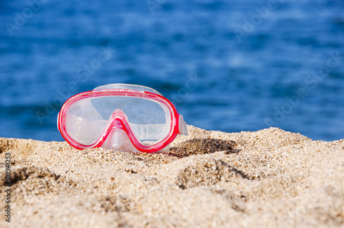 Diving mask on the sand of a beach, blue water in the background