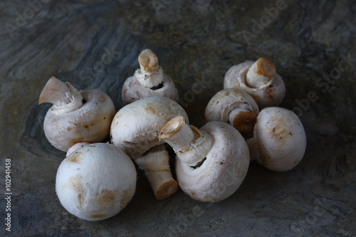 Many small raw unpeeled white champignons with round hats and short stems on brown wooden table