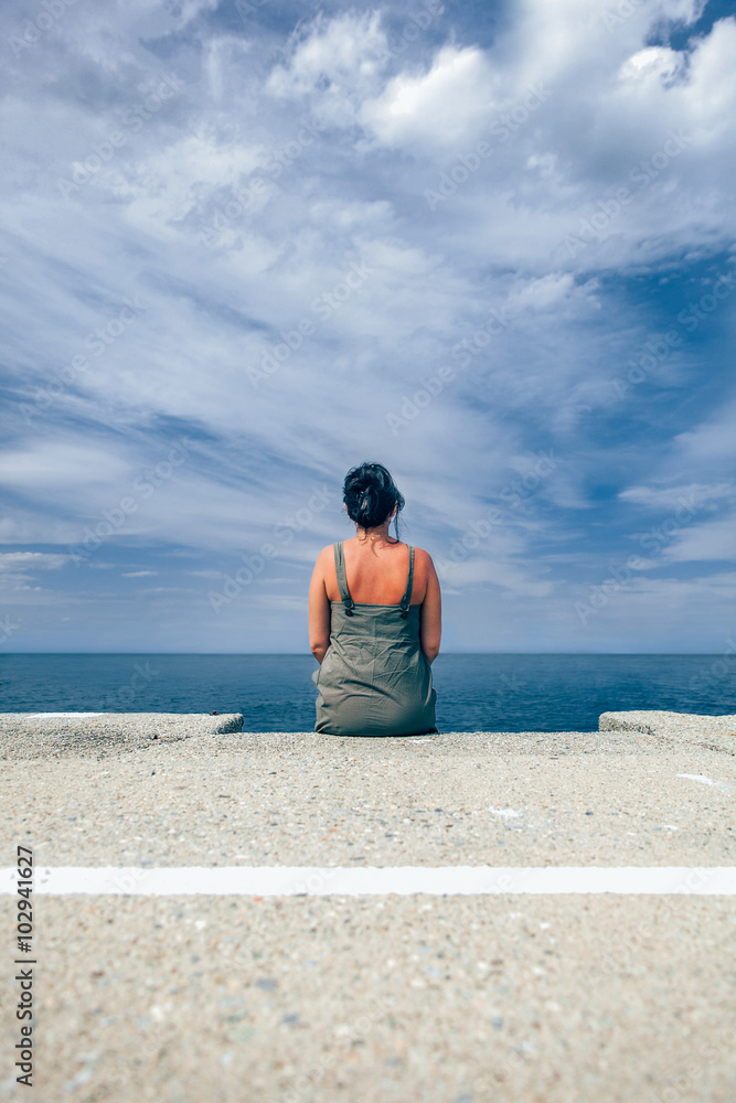 Woman sitting on the dock watching the sea Woman sitting on the dock watching the sea