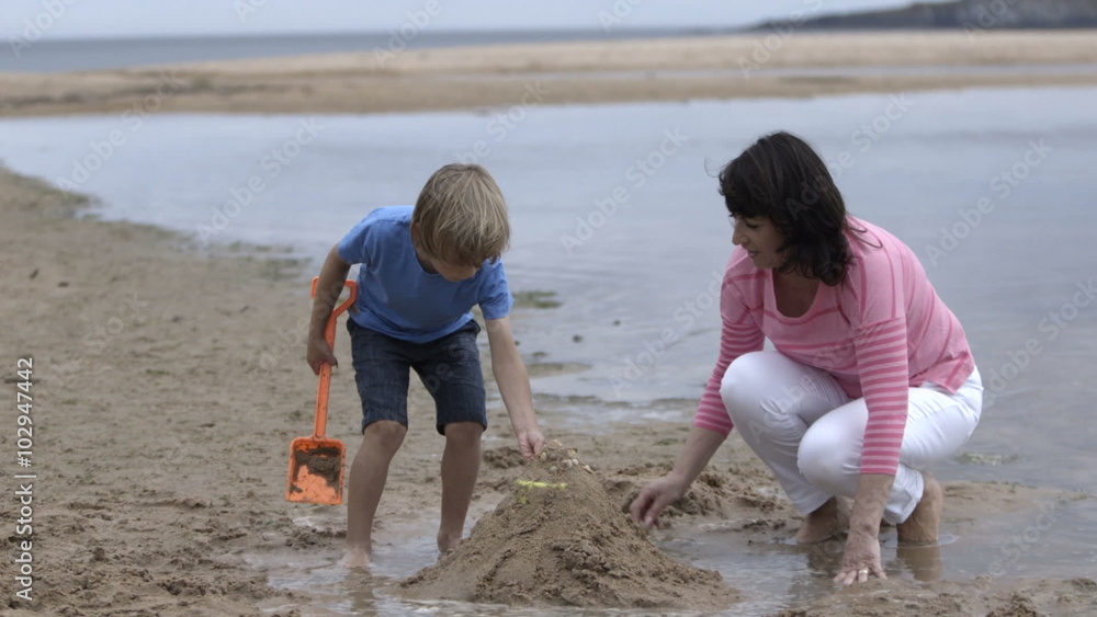 A grandmother and her grandson are at the beach. They are making sand castles and searching for little shells in the sand. A grandmother and her grandson are at the beach. They are making sand castles and searching for little shells in the sand.