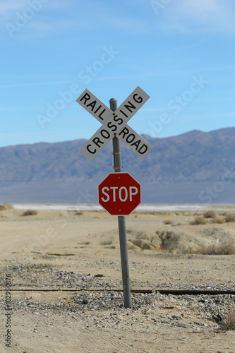 Railroad Crossing Stop Sign / A railroad crossing sign with a stop sign underneath in the desert with mountains in the background on a semi cloudy and clear day.