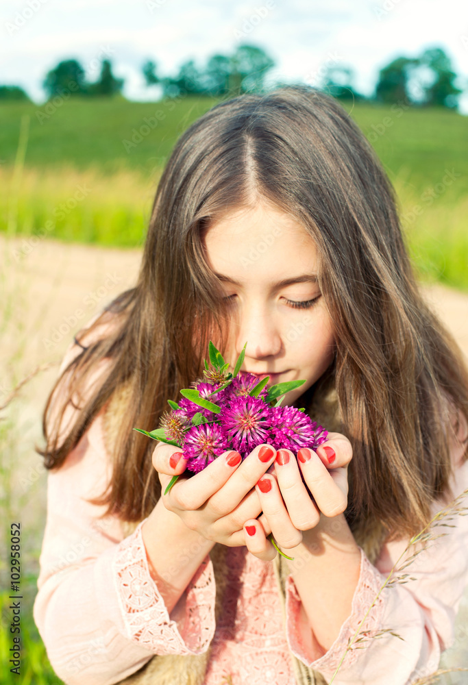 Fototapeta premium Beauty of nature. Smiling young girl smelling meadow clover flow