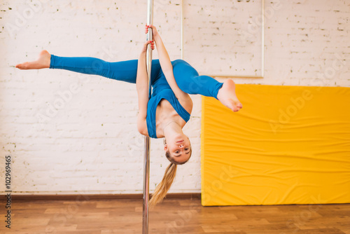 girl in a blue dress in the gym on a pole splits, exercise on a pole