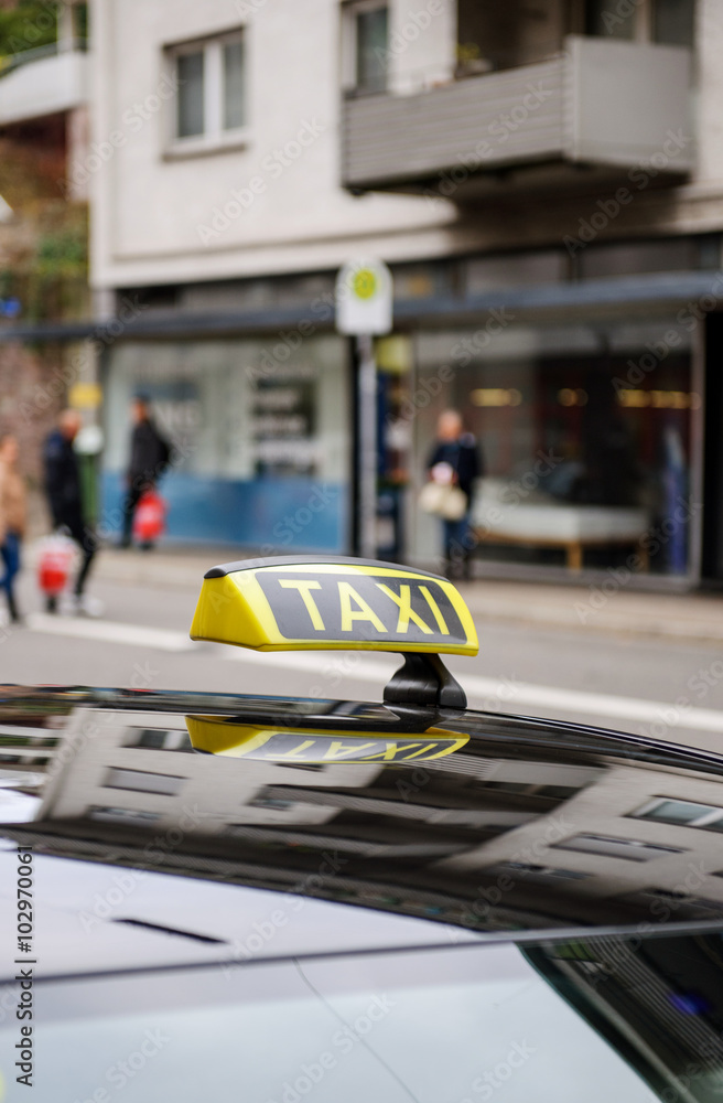 Obraz premium Taxi sign waiting for customers in city with defocused pedestrians and city background 