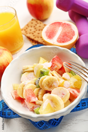 Fruit salad and dumbbells on wooden background. Healthy eating concept.