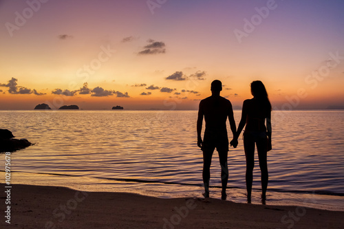 Young couple standing on the beach holding hands and watching tropical sunset