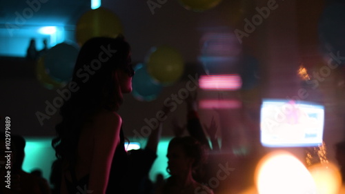 Young attractive girl is dancing at a costume party in the club. People are hanging out on a dancefloor. 