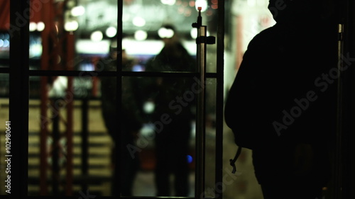 Person walking into the building through a glass door; security guards are inside the house on a background. 