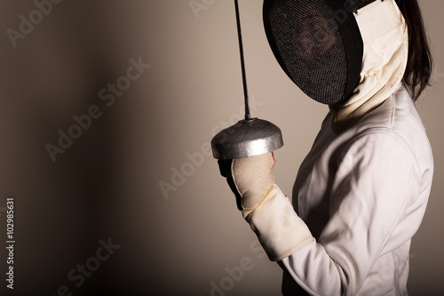 Portrait of woman wearing white fencing costume practicing with the sword.
